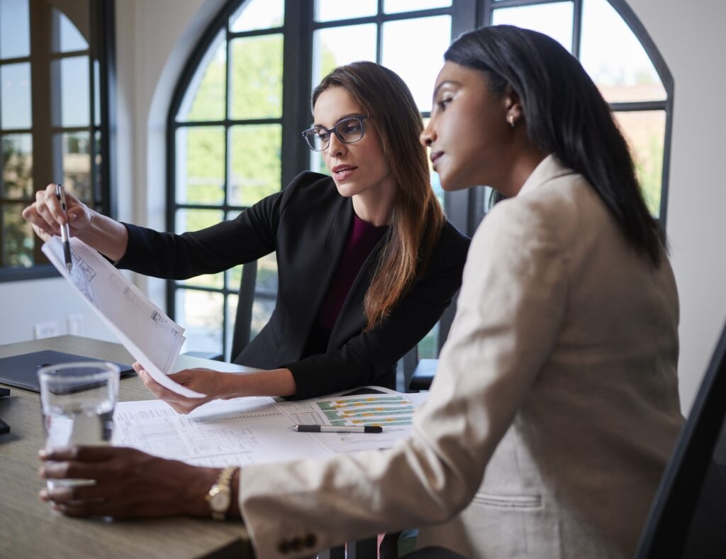 Two businesswomen sitting at a conference table going over paperwork together.