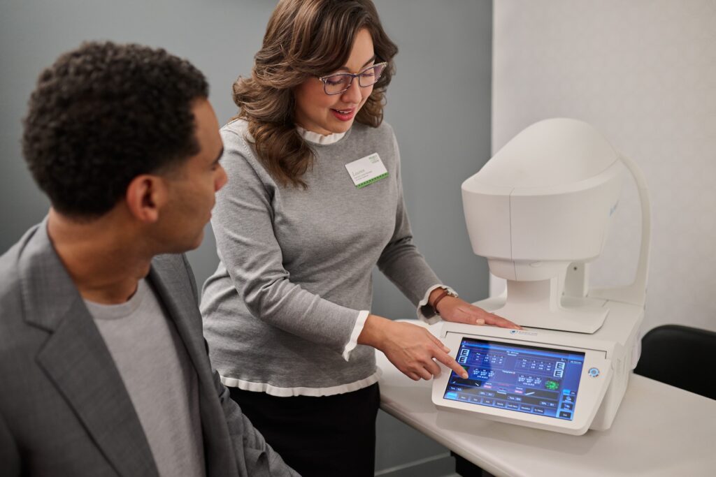 Woman showing man how a touch screen optometrist machine works.