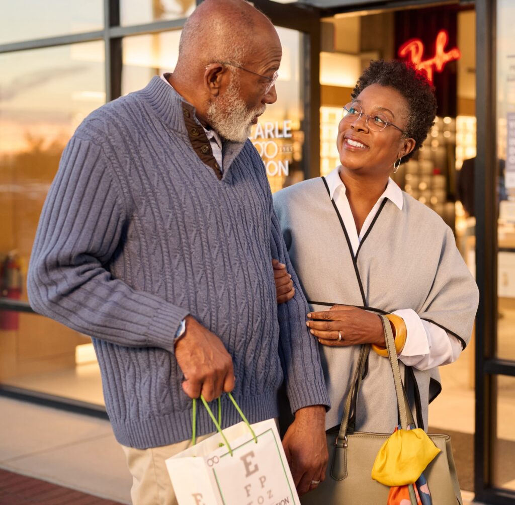 Elderly couple smiling and holding hands while walking out of a pearle vision location.